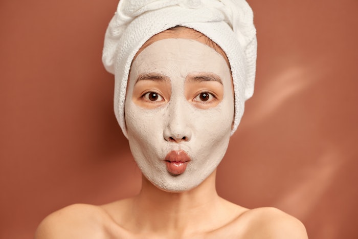Young woman practicing self-care with a clay face mask.