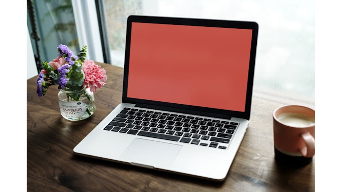 A computer sits on a table with a coffee mug and a flower vase.